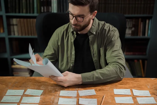 Adult male studying papers in a library setting, focusing on education and research. Building Quebec celebrity trivia in French and English without flattening the star system