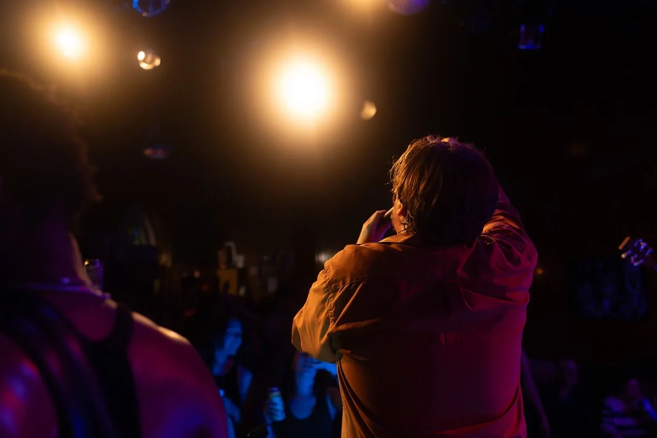concert, singer, audience, stage, spotlight, orange, show, room, live music, entertainment, fans, atmosphere, music, microphone, energy, evening, podium, artist, performance, party, club. US Quiz Nights That Ask About Canadian Celebrity Deaths and Obituaries